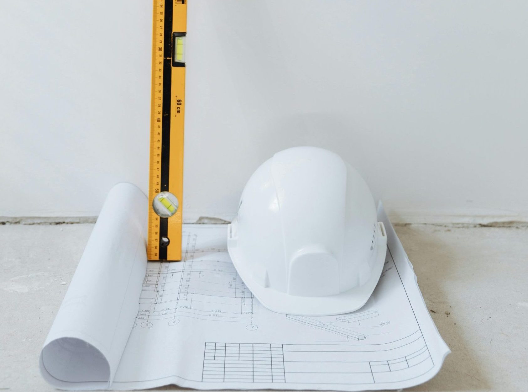 Rolled blueprint, hard hat, and level tool arranged against a white background.